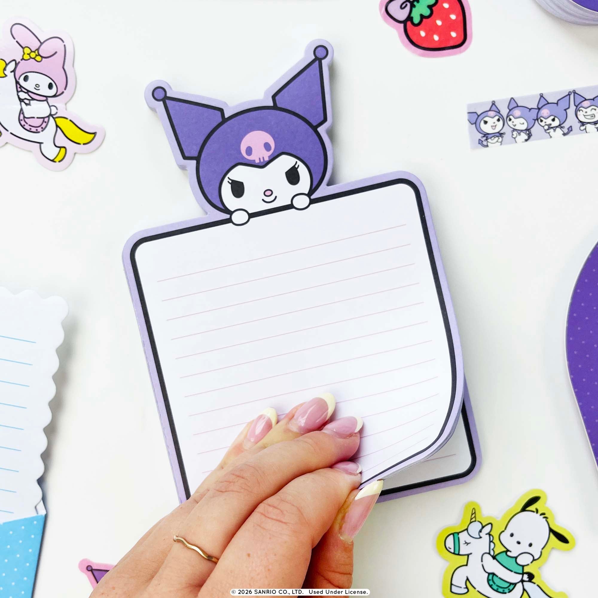A hand holds a Kuromi-themed notepad with lined writing space, surrounded by other Sanrio character stickers on a white background.